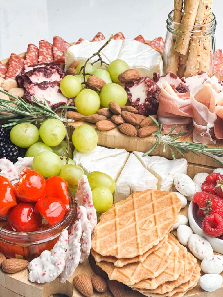 close up image of a cheeseboard featuring nuts, crackers, meats and herbs
